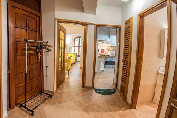 A hallway with a wooden door, a rack with hanging items, and a welcome mat.