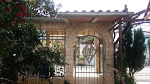 Una entrada de piedra con una reja de metal, plantas en macetas y una pequeña escalera que lleva a una puerta con un letrero en forma de diamante.