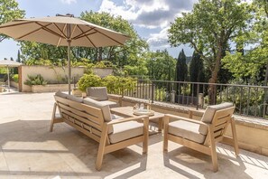 Ein Außenbereich mit Sitzgelegenheiten, darunter eine Couch und Stühle, sowie ein Tisch und ein großer Sonnenschirm.