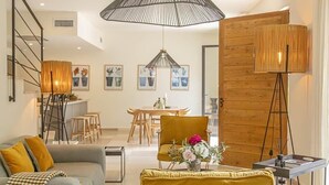 Ein modernes Wohnzimmer mit einer Couch, einem gelben Sessel, einem Essbereich und einer großen Pendelleuchte.