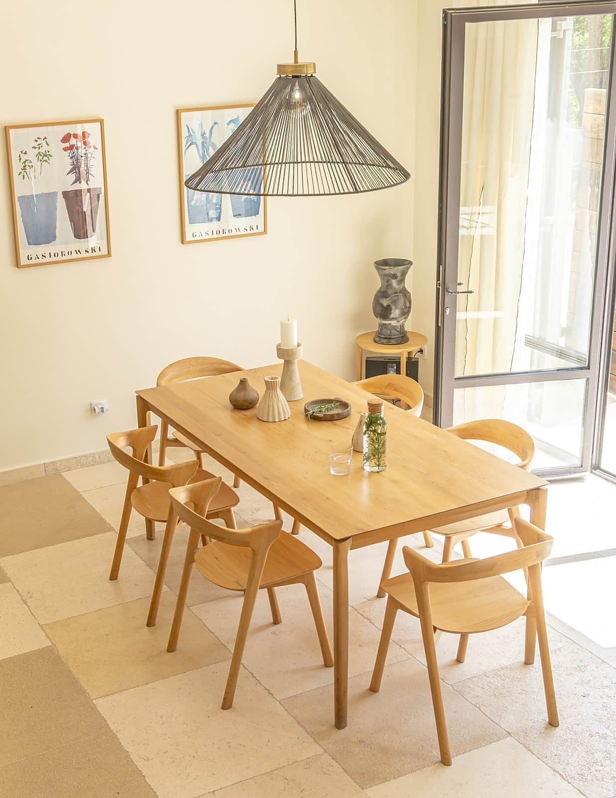 A dining area with a wooden table, six chairs, a hanging pendant light, and two framed artworks on the wall.