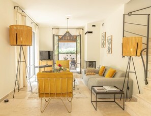 A living room with a sofa, coffee table, floor lamp, and a TV. - Bastide du Couchant du Mas de l'Amarine (ST REMY DE PROVENCE)