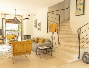 Ein modernes Wohnzimmer mit einer Couch, einem Couchtisch und einer Stehlampe. Eine Treppe mit Metallgeländer und ein an der Wand befestigtes Kunstwerk sind ebenfalls zu sehen.