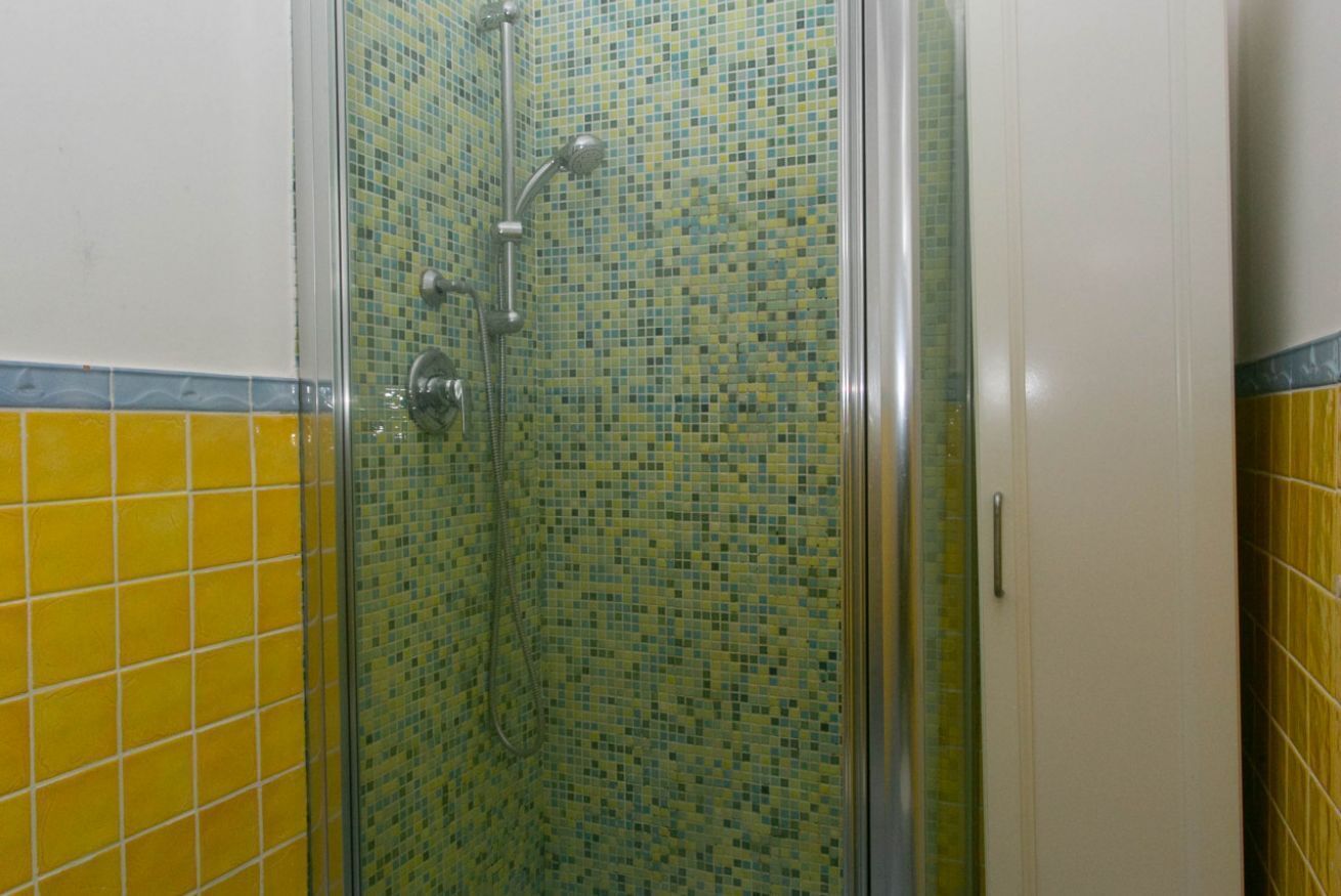 Una doccia con porta in vetro e pareti rivestite di mosaico.