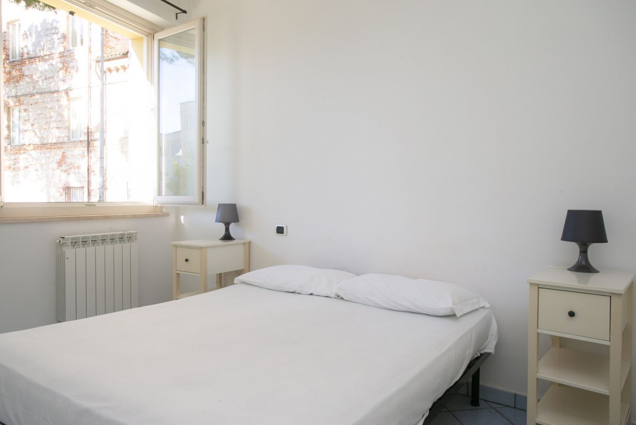 Ein Schlafzimmer mit einem Bett, zwei Nachttischen, einem Fenster und einer Heizung.