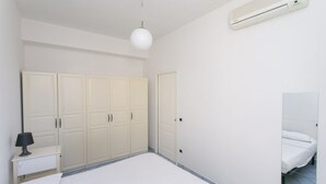 Een slaapkamer met een bed, nachtkastje met lamp, kledingkast en een airconditioning.