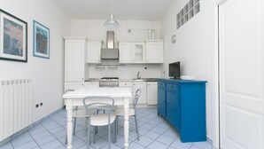 Een keuken met witte kasten, een blauw aanrecht, een eettafel met stoelen en een hangende lamp.