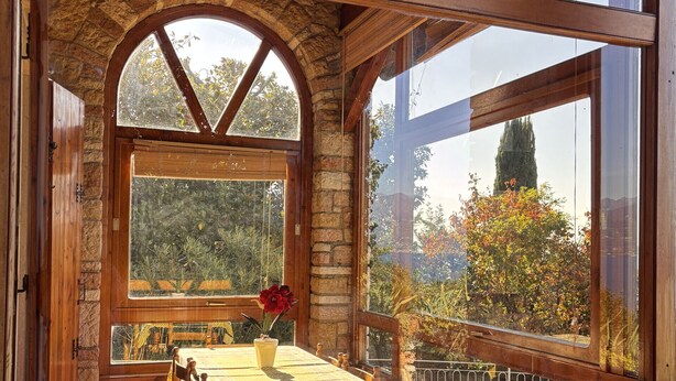A wooden cabin with a stone wall, a wooden table with chairs, and a view of trees and a mountain. - Villa Margiò (Torri del Benaco)