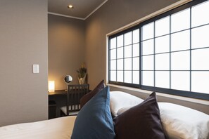 Une chambre d’hôtel avec une grande fenêtre, un bureau avec une lampe et une chaise.