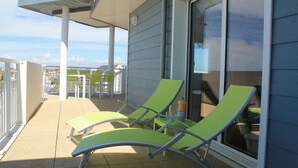 A balcony with two green lounge chairs, a table, and a bottle of orange juice.
