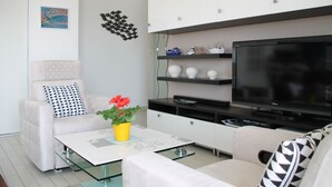 A modern living room with a sofa, coffee table, and TV. There are decorative items on shelves and a potted plant on the coffee table.