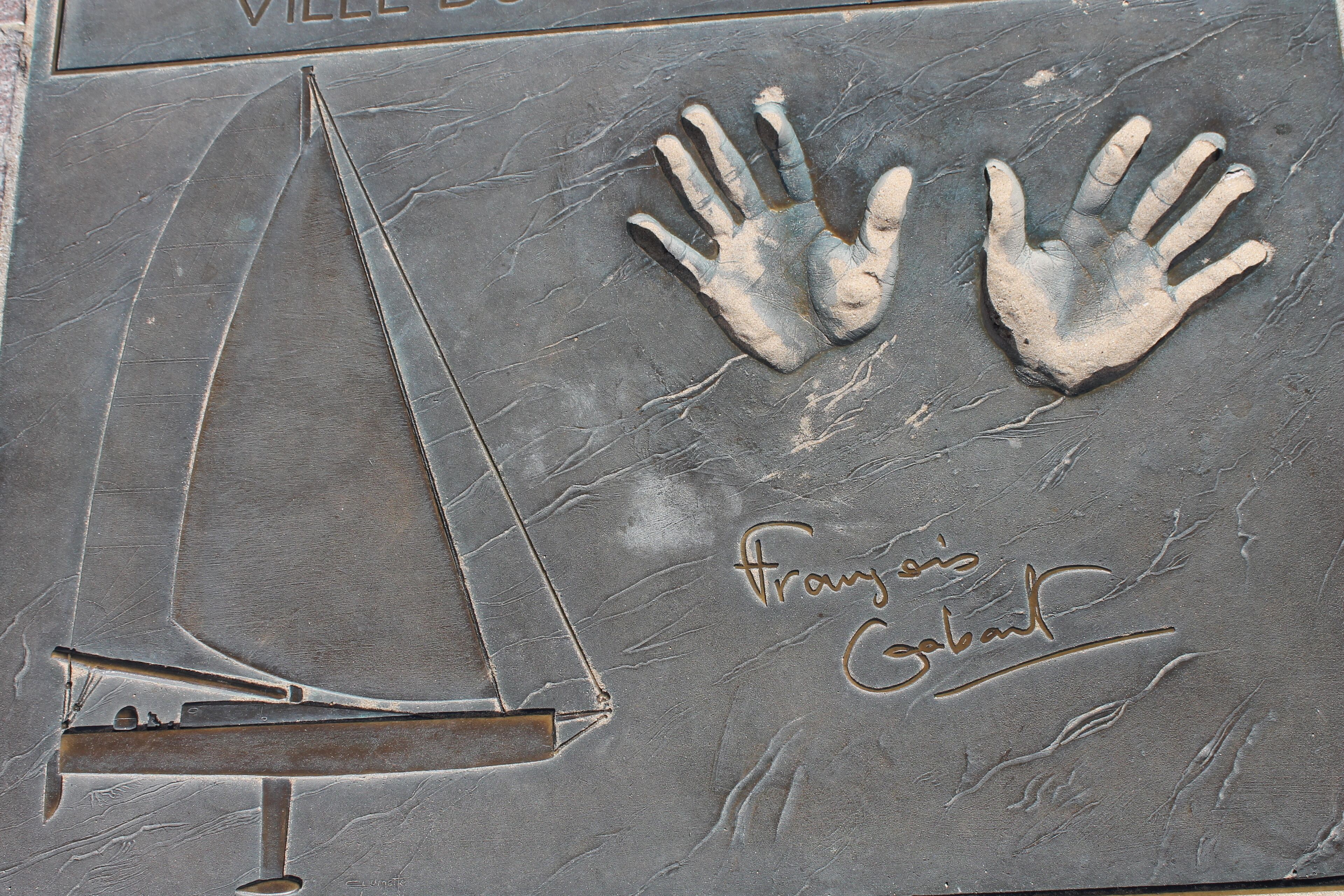 A stone surface with a sailboat and two handprints, and the text 'Franzis Galat' engraved.