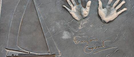 A stone surface with a sailboat and two handprints, and the text 'Franzis Galat' engraved.
