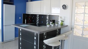 A kitchen with a central island, white cabinets, a black tiled backsplash, and a clock on the wall.