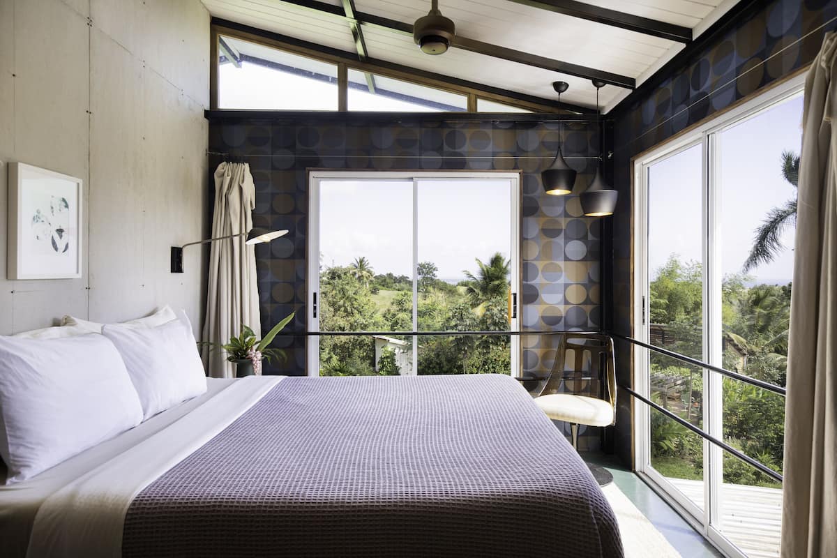 A bedroom with a large bed, a view of greenery outside, and a balcony with a railing.