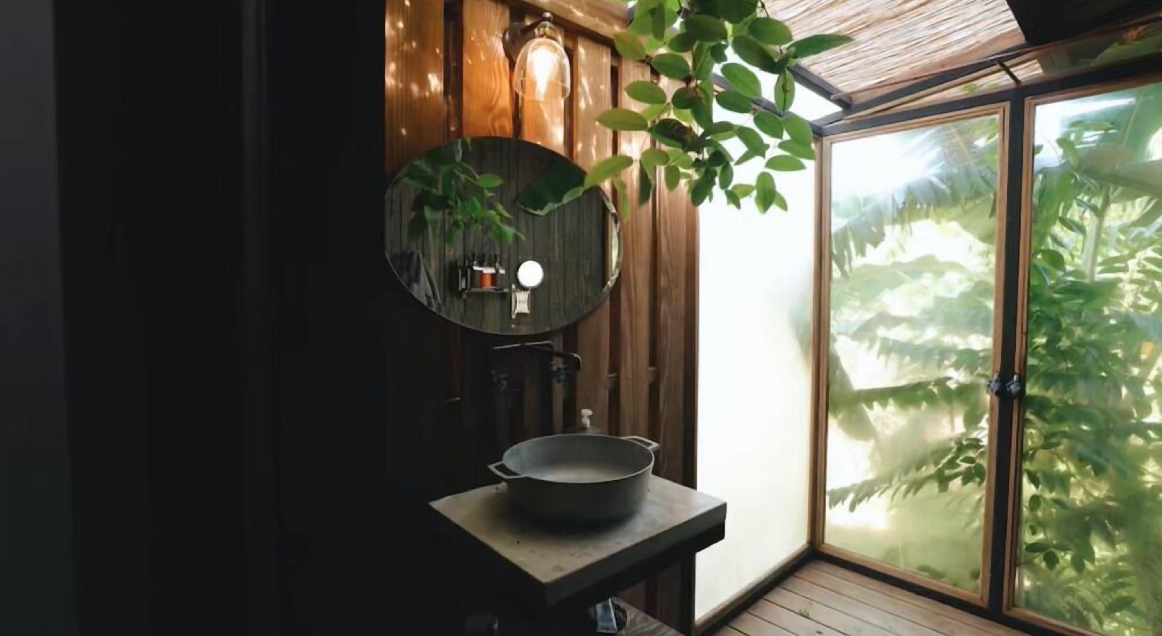 Un baño con tocador de madera, un espejo redondo y una ventana con vistas a zonas verdes.