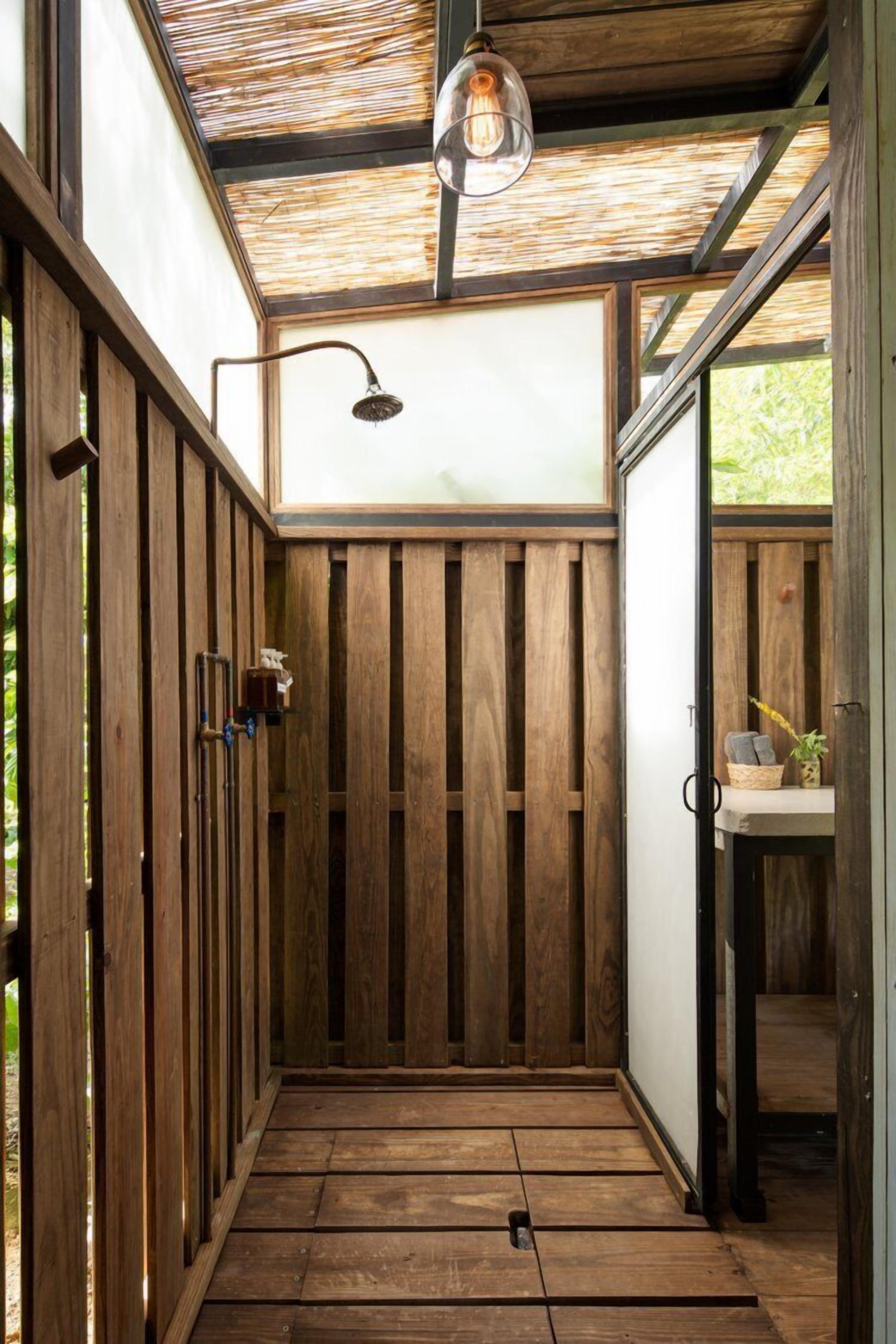 A wooden shower enclosure with a glass door, a hanging light fixture, and a small table with a plant.