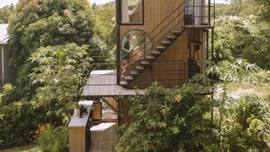 A wooden cabin with a deck, a staircase, and a small outdoor seating area surrounded by greenery. - Finca Victoria (Vieques)