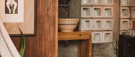 A rustic bathroom with a wooden vanity, a large mirror, and a concrete wall with square recesses.