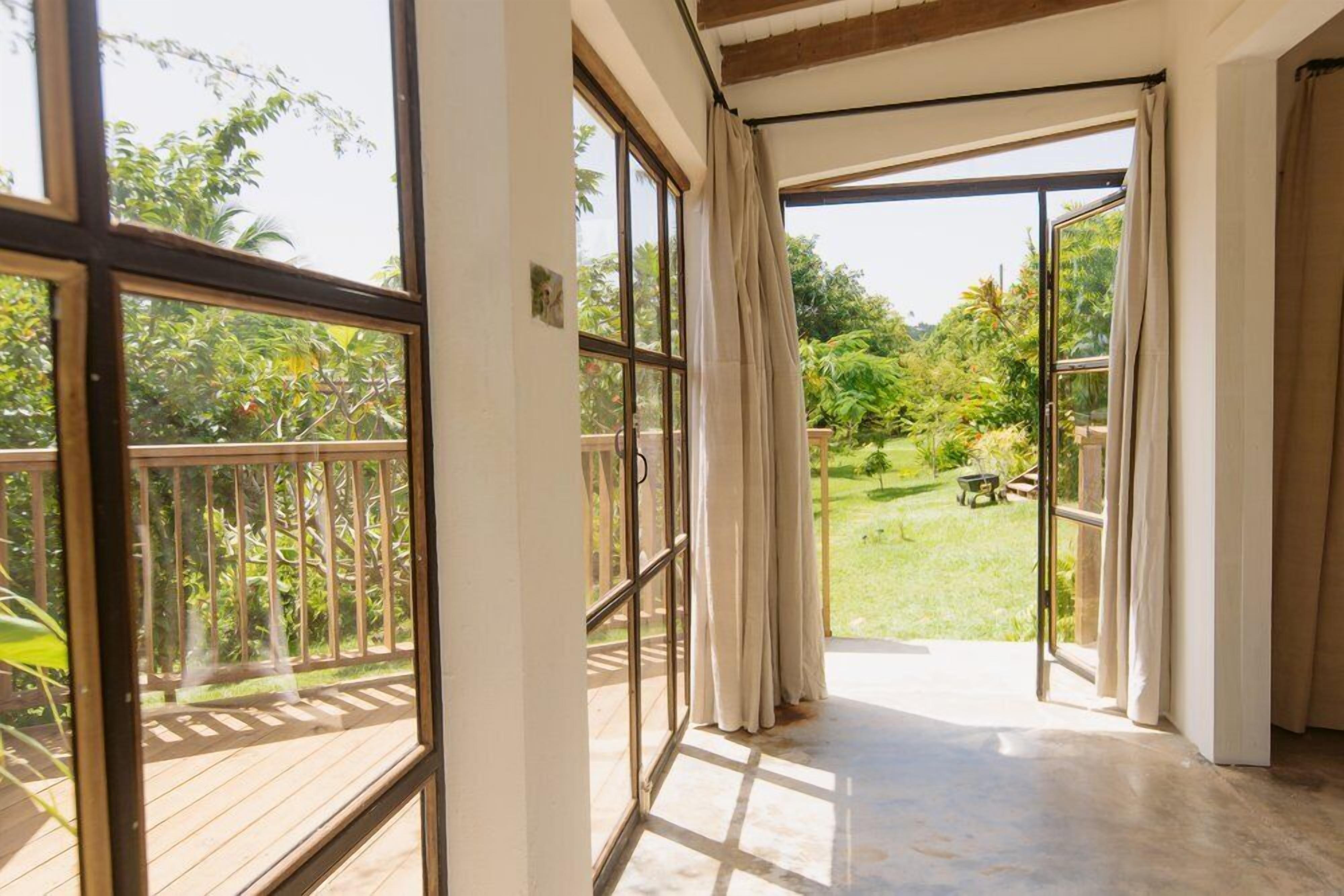 A room with large windows, a wooden deck, and a view of a garden.