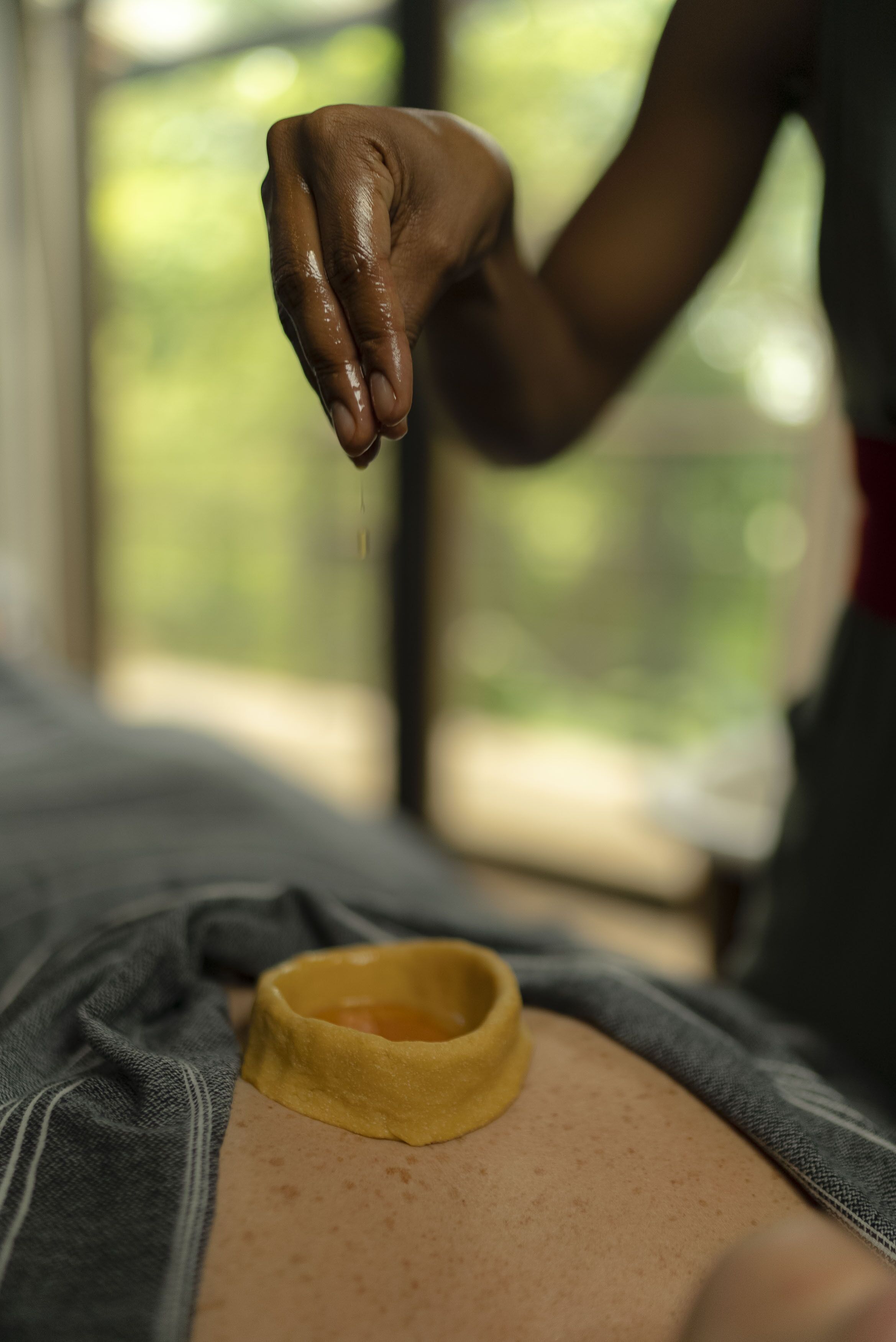 Une personne reçoit un massage, et on peut voir un récipient contenant de l’huile jaune sur son dos.