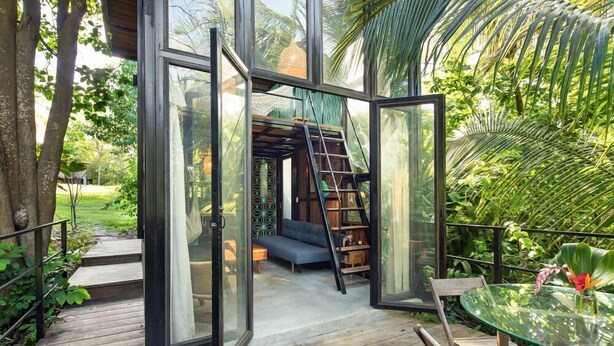 An open glass door leading to a cozy interior with a sofa, a ladder, and a dining area with a glass table and chairs. - Finca Victoria (Vieques)