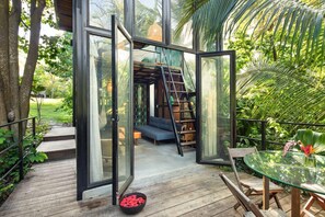 Una puerta de cristal abierta que da a un interior acogedor con un sofá, una escalera y un comedor con mesa y sillas de cristal.