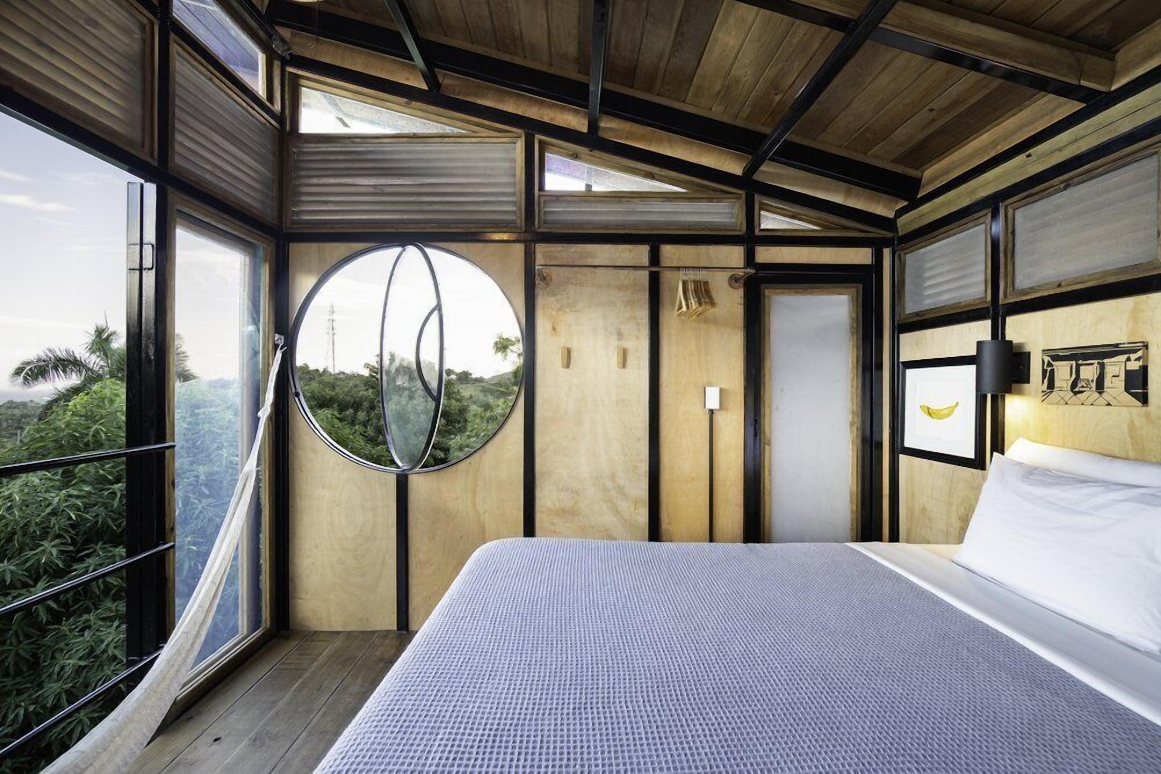 A modern bedroom with a large bed, a circular window, and a view of greenery outside.