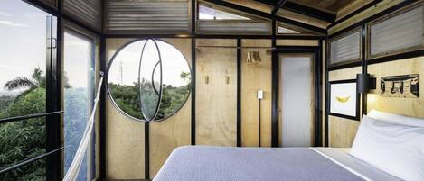 A modern bedroom with a large bed, a circular window, and a view of greenery outside.