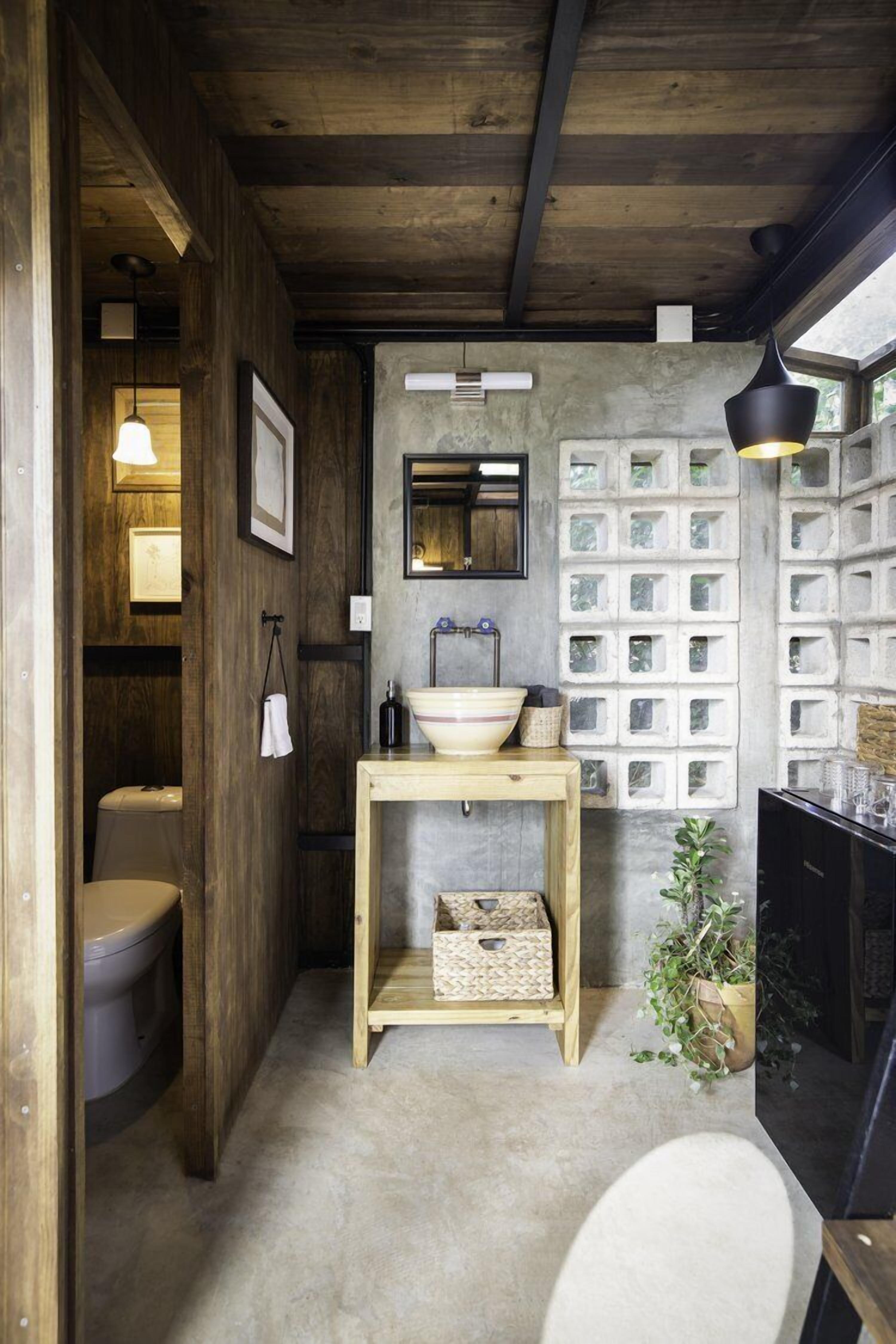 A bathroom with a wooden ceiling, a sink with a basin, a mirror, and a wall with square windows.