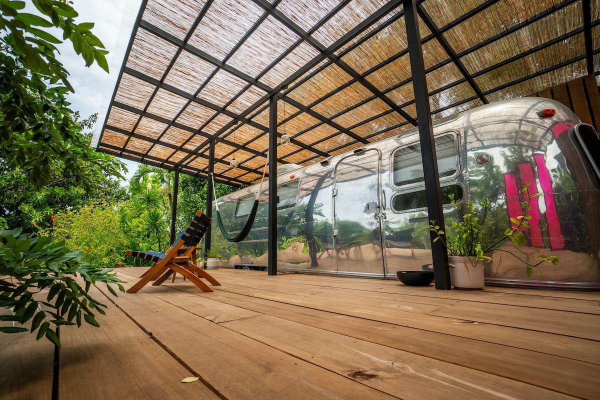 A train parked under a wooden deck with a metal roof, surrounded by greenery.
