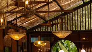 A restaurant interior with a high ceiling, hanging lights, and a central mirror reflecting greenery. - Finca Victoria (Vieques)