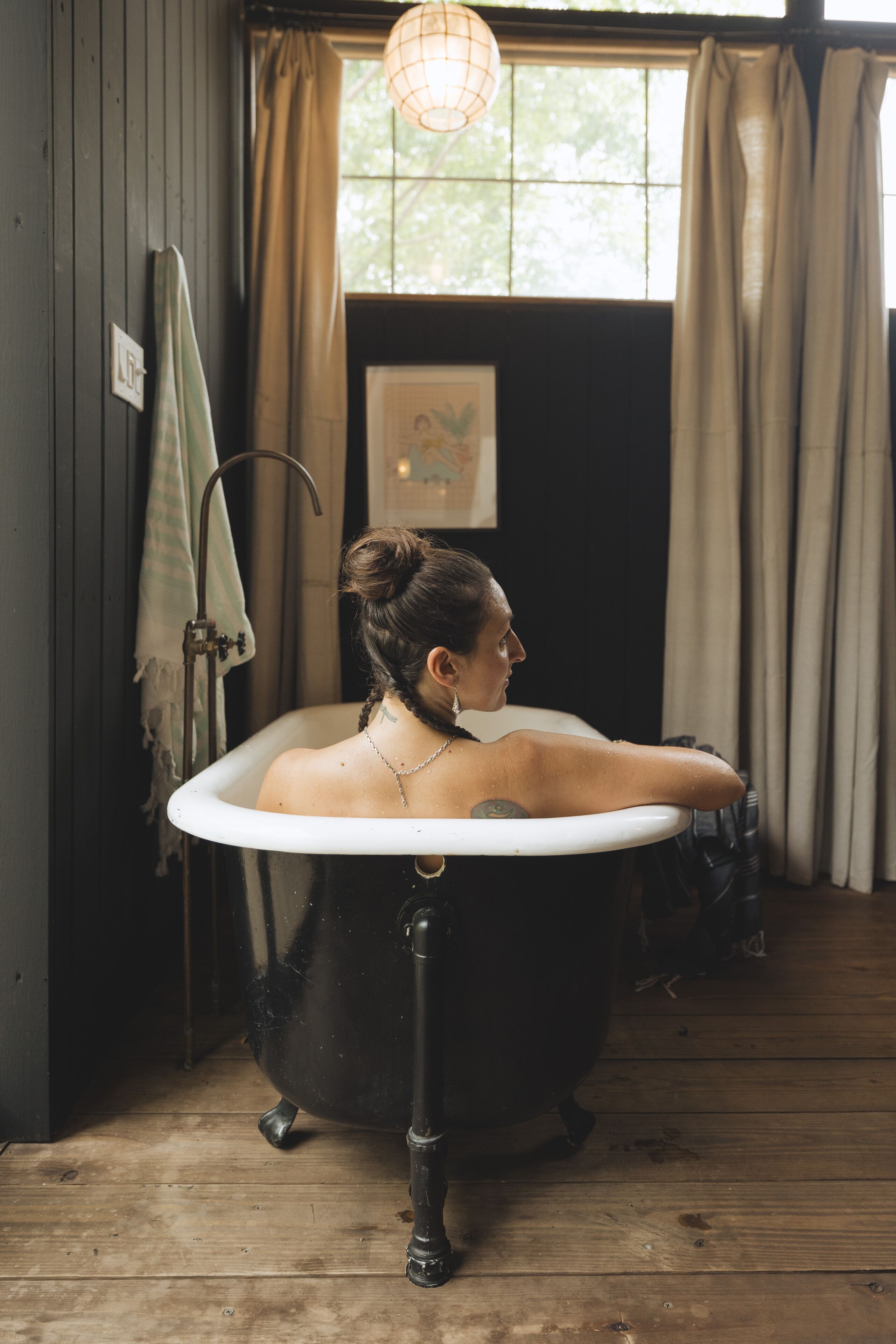 A vintage bathtub in a rustic bathroom with wooden floors and a window with curtains.