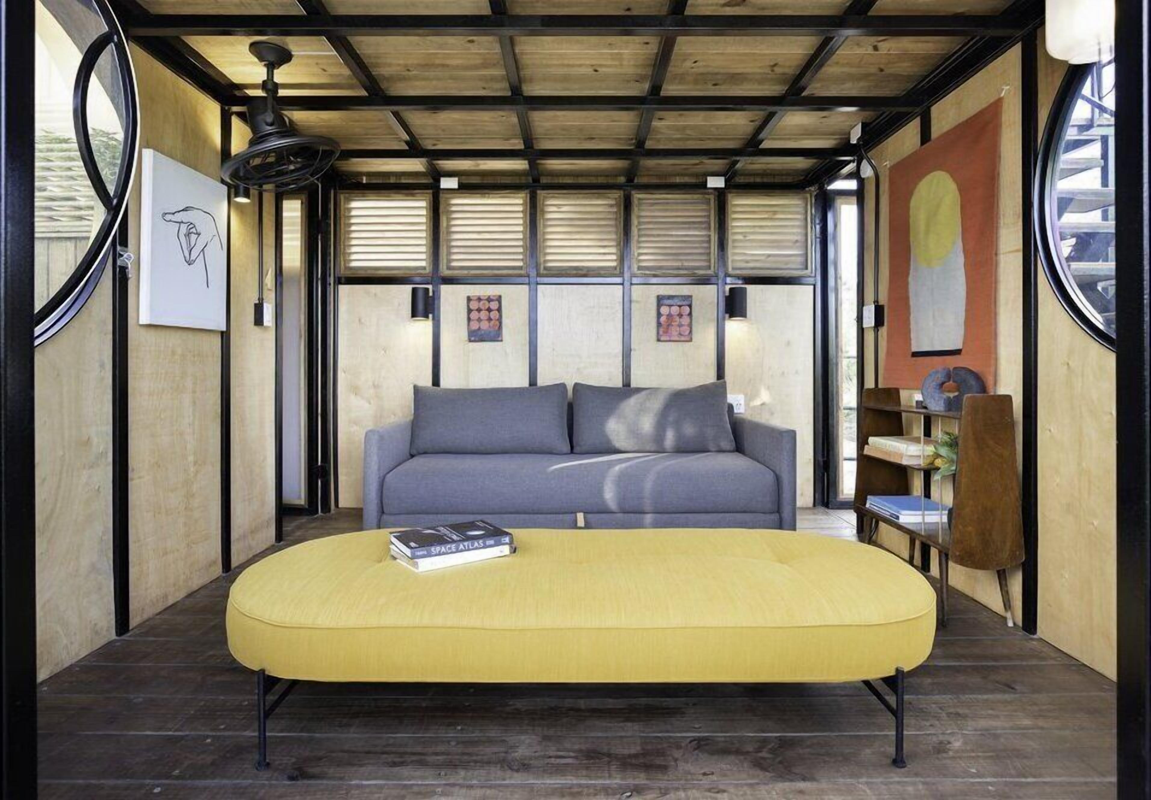 A modern interior with a sofa and ottoman, wooden beams, artwork, and a bookshelf.