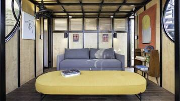 A modern interior with a sofa and ottoman, wooden beams, artwork, and a bookshelf.