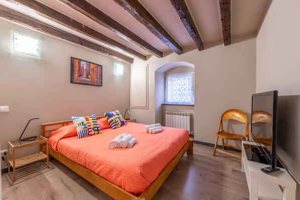 Un dormitorio con una cama de madera, almohadas coloridas, un televisor y una ventana con cortinas estampadas.