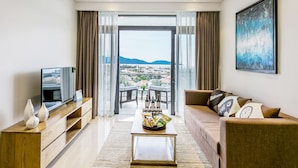 Ein modernes Wohnzimmer mit Fernseher, Holzmöbeln, einem Couchtisch mit Zeitschriften und einem Balkon mit Blick auf die Stadt.