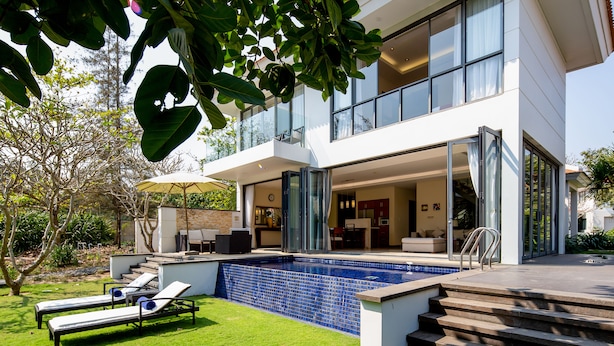 Ein modernes Haus mit Schwimmbad, Außenbereich mit Sitzgelegenheiten und einer großen Glasdoor, die zum Innenraum führt.