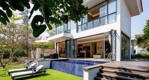 Une maison moderne dotée d’une piscine, d’un espace salon extérieur et d’une grande porte vitrée donnant sur l’intérieur.