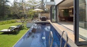 Un espace piscine extérieur moderne, doté d’un patio fermé par des baies vitrées et d’une pelouse bien entretenue.