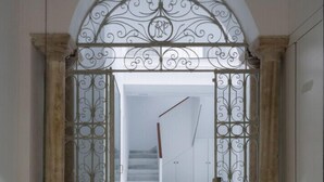 Un arcoado de entrada con ornamentada rejería que da a una escalera.