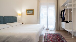 A hotel room with a bed, a nightstand, a lamp, a painting, a wardrobe, and a window with curtains. - La Cagliaritana - Attic in the city center  (Cagliari)