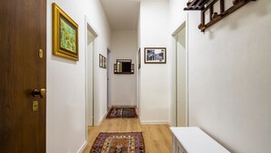 A narrow hallway with wooden floors, white walls, and a white door at the end. There are two rugs on the floor and two framed pictures on the walls. - La Cagliaritana - Attic in the city center  (Cagliari)