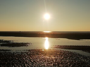 A beach scene with the sun low on the horizon, reflecting on the wet sand.