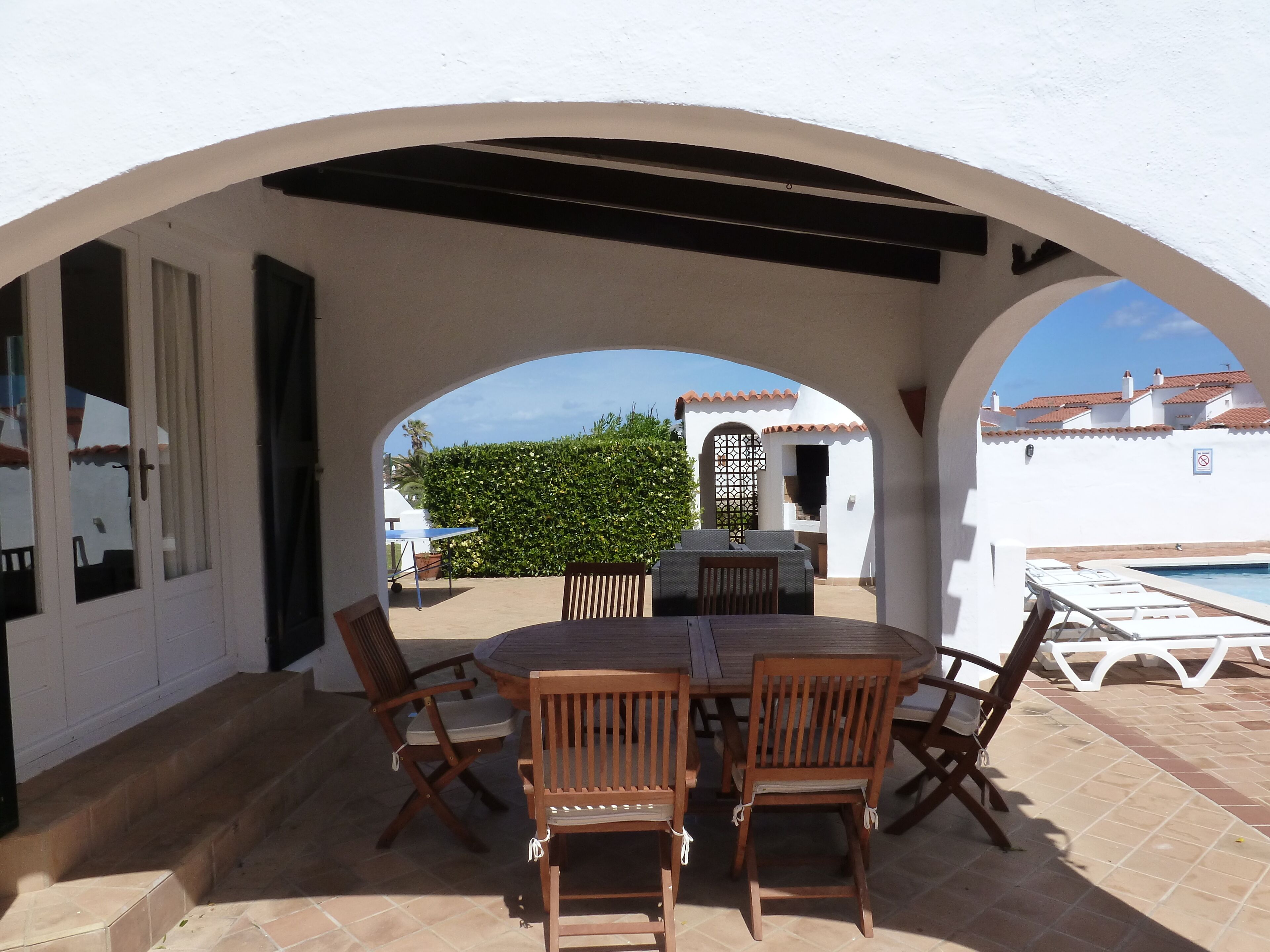 Une terrasse extérieure avec une table et des chaises, une piscine et une vue sur les bâtiments en arrière-plan.