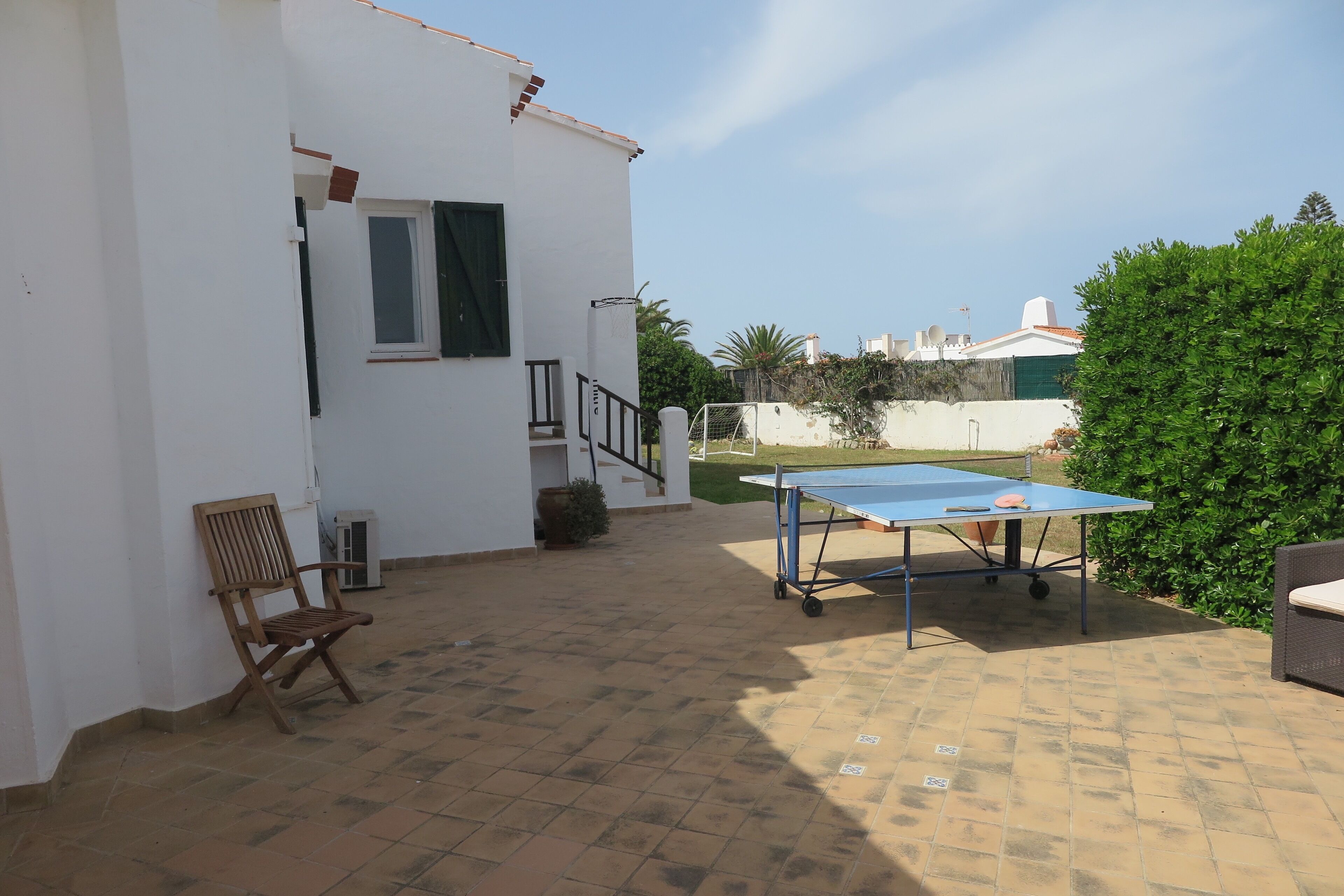 A patio area with a ping pong table, a wooden chair, and a staircase leading to an upper level.