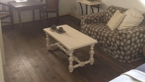 A cozy room with a wooden floor, a white table with a lamp, a patterned sofa, and a small table with a pitcher. - Chambre Gras - Chateau Serre Barbier (Saint-Béat)