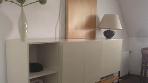 A white cabinet with a shelf, a lamp, and a vase with green leaves. - Chambre Gras - Chateau Serre Barbier (Saint-Béat)