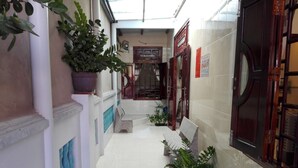 Un couloir étroit au sol carrelé, avec des bancs, des plantes en pot et des portes en bois.