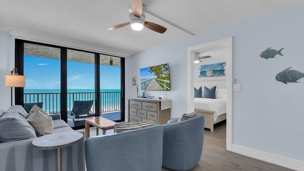 A modern room with a balcony, a bed, a sofa, and a TV. - SEA WINDS 504 - Direct Gulf Views from Coastal Renovated Beachfront Condo! (Marco Island)
